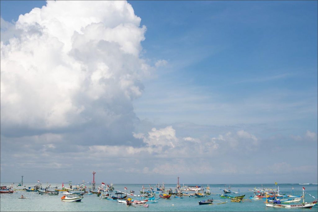Bali Uluwatu wedding: colourful traditional fishing boats dotted towered by a cloud.