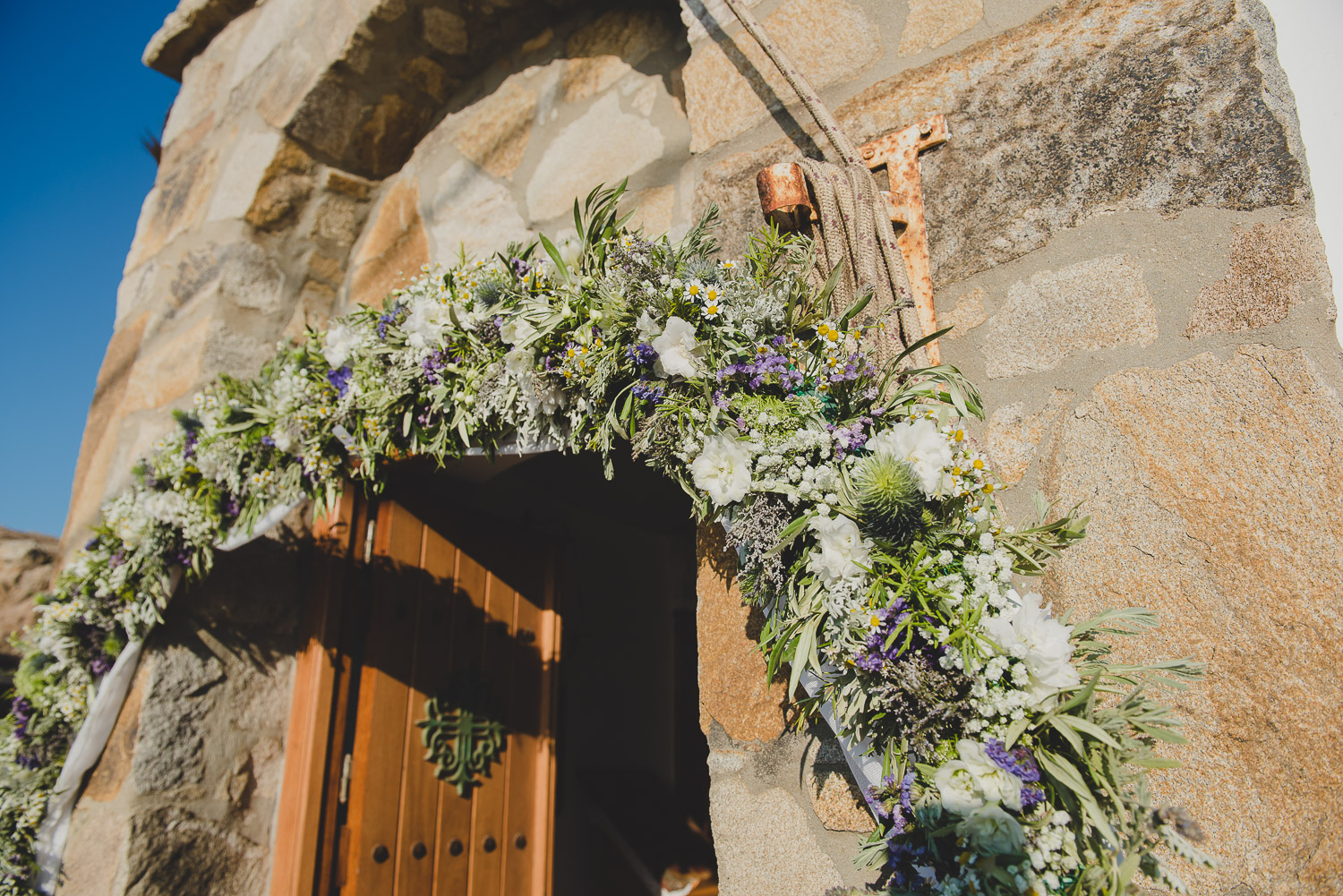 Wedding photographer Mykonos: church entrance adorned in wild flowers at Mykonos wedding.