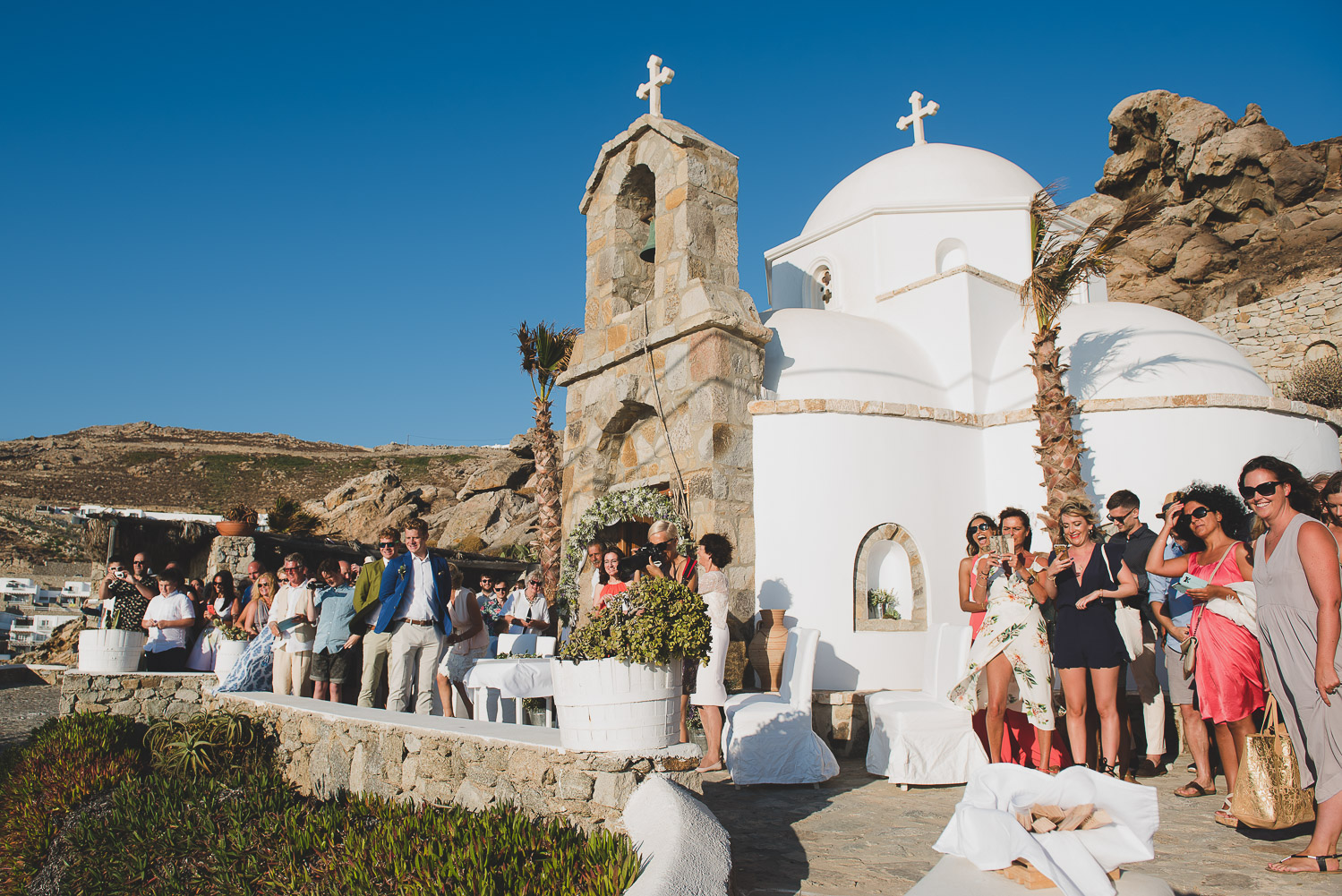 Wedding photographer Mykonos: guests at church waiting for the bride for Mykonos wedding.