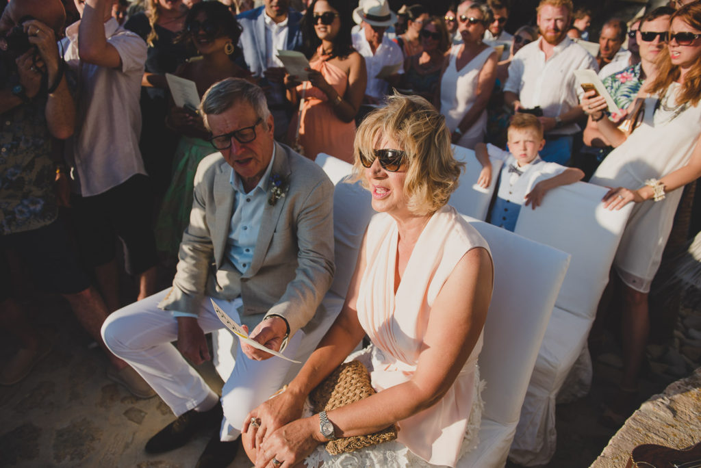 Wedding photographer Mykonos: parents singing during Mykonos wedding church surrounded by guests.