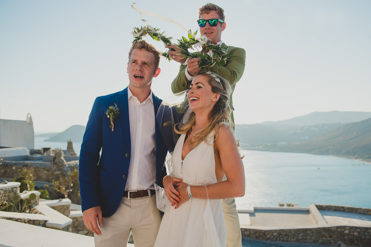 Wedding photographer Mykonos: best man holds olive branch wedding crowns above couple's heads during  Mykonos wedding.