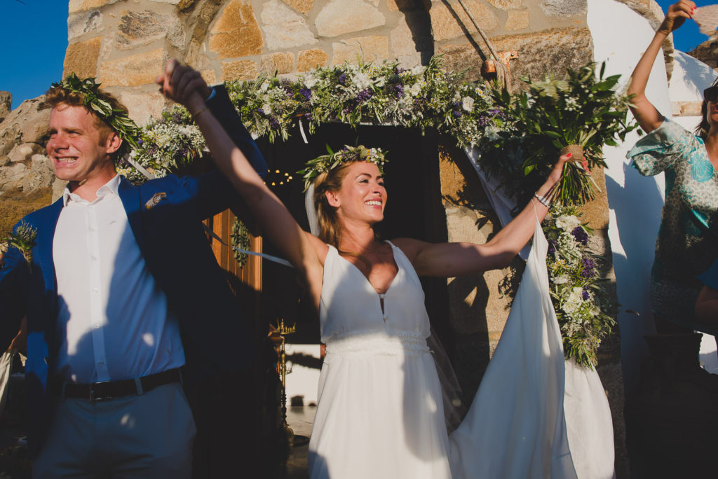Wedding photographer Mykonos: newlyweds with hands in the air smiling during their Mykonos wedding.