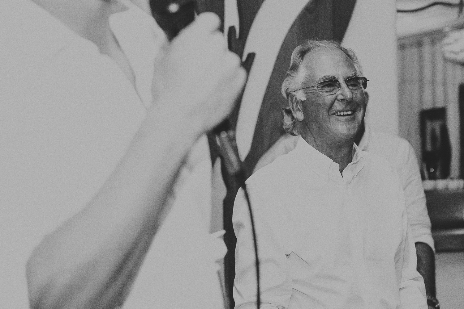 Wedding photographer Mykonos: black and white photo of the father of the bride laughing at Elia during Mykonos wedding speeches.
