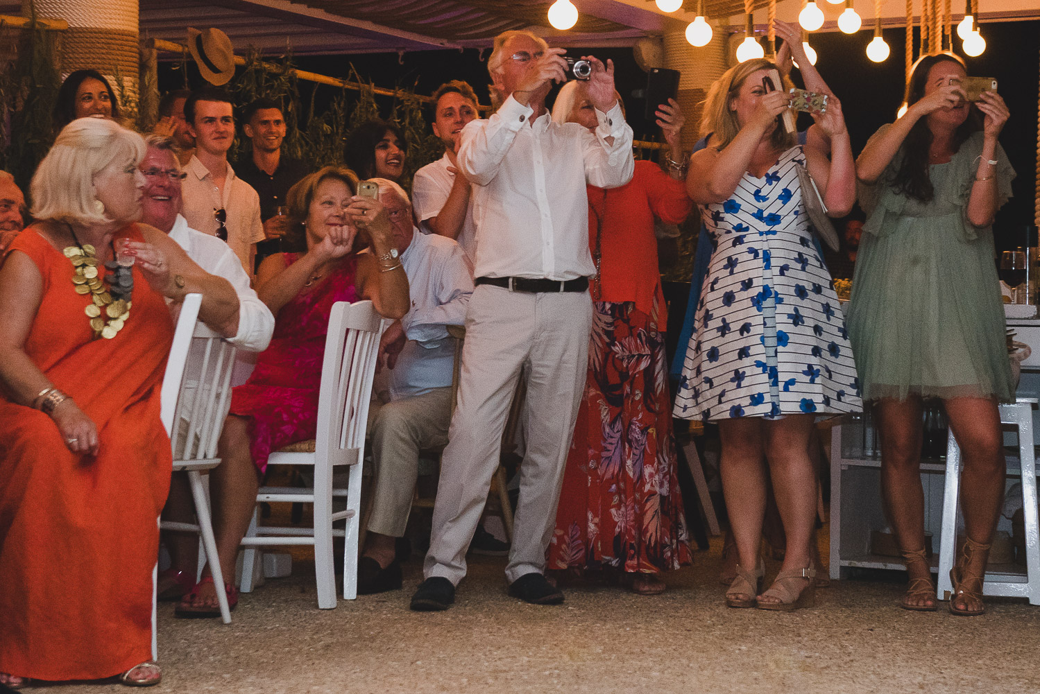 Wedding photographer Mykonos: guests cheering bride and groom at Elia during Mykonos wedding reception.