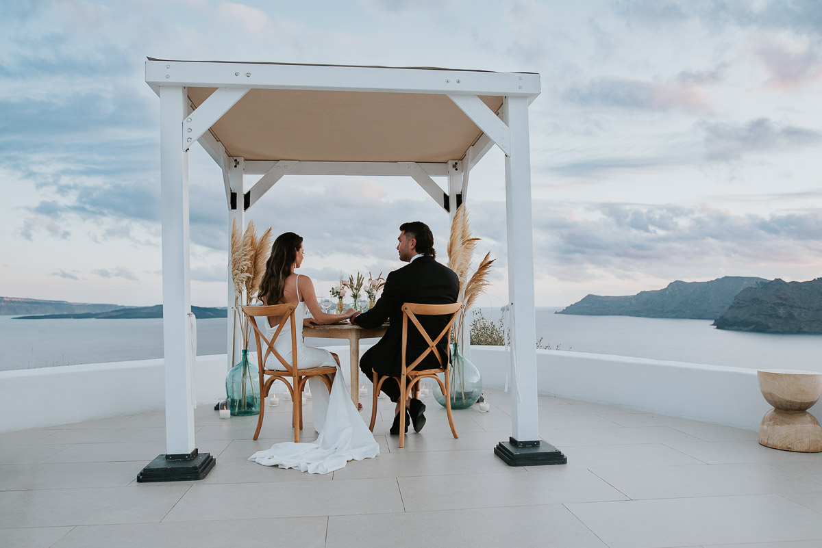 Santorini elopement photographer: couple under gazebo with the dinner views by Ben and Vesna.