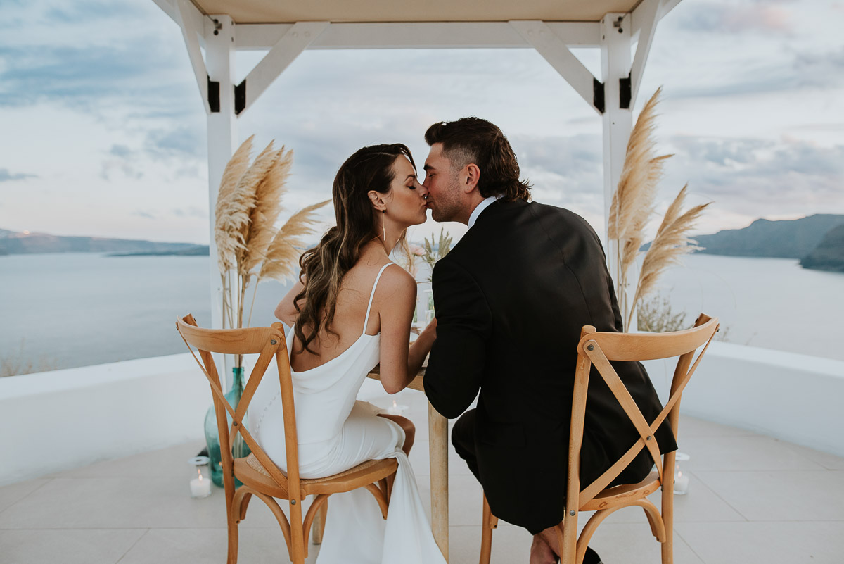 Santorini elopement photographer: couple kissing at the dinner table by Ben and Vesna.