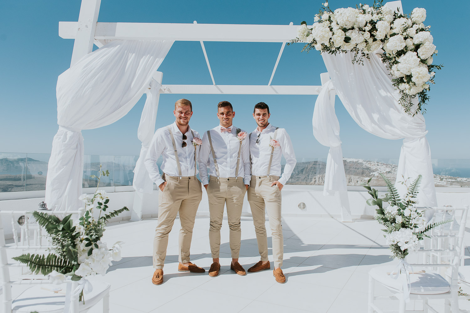 Wedding photographer Santorini: groom and groomsmen under gazebo covered in flowers by Ben and Vesna.