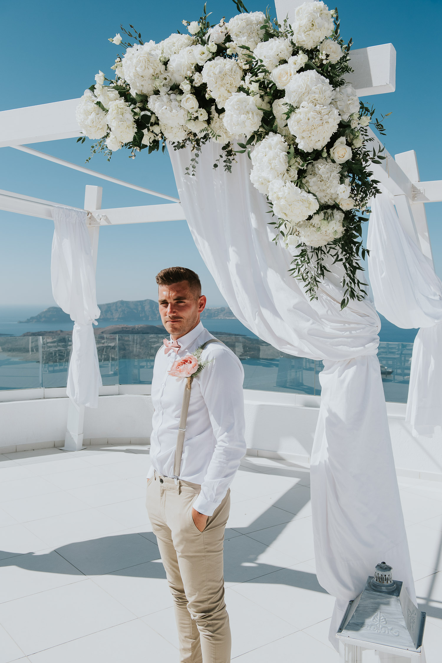 Wedding photographer Santorini: close up of groom under gazebo covered in flowers by Ben and Vesna.