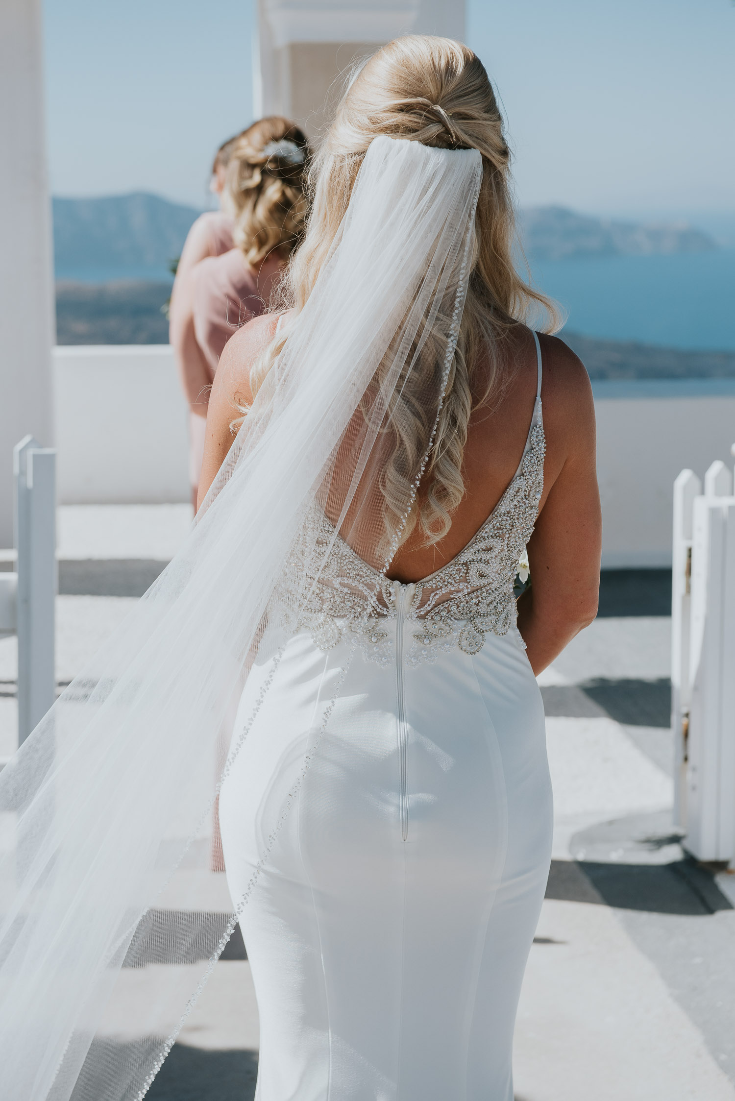 Wedding photographer Santorini: the back of the bride her dress with the veili in the wind by Ben and Vesna.