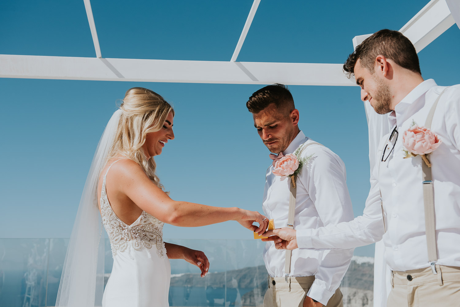 Wedding photographer Santorini: bride smiling as she takes a wedding ring from the best man by Ben and Vesna.
