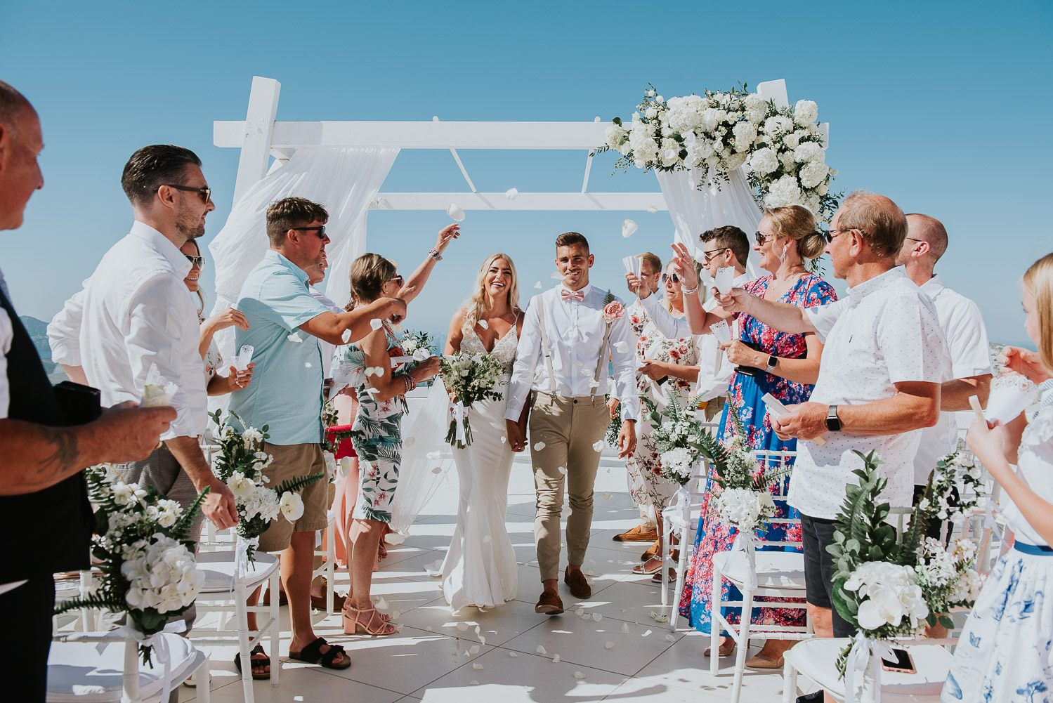 Wedding photographer Santorini: bride and groom laughing walking down the aisle showered in rose petals by Ben and Vesna.