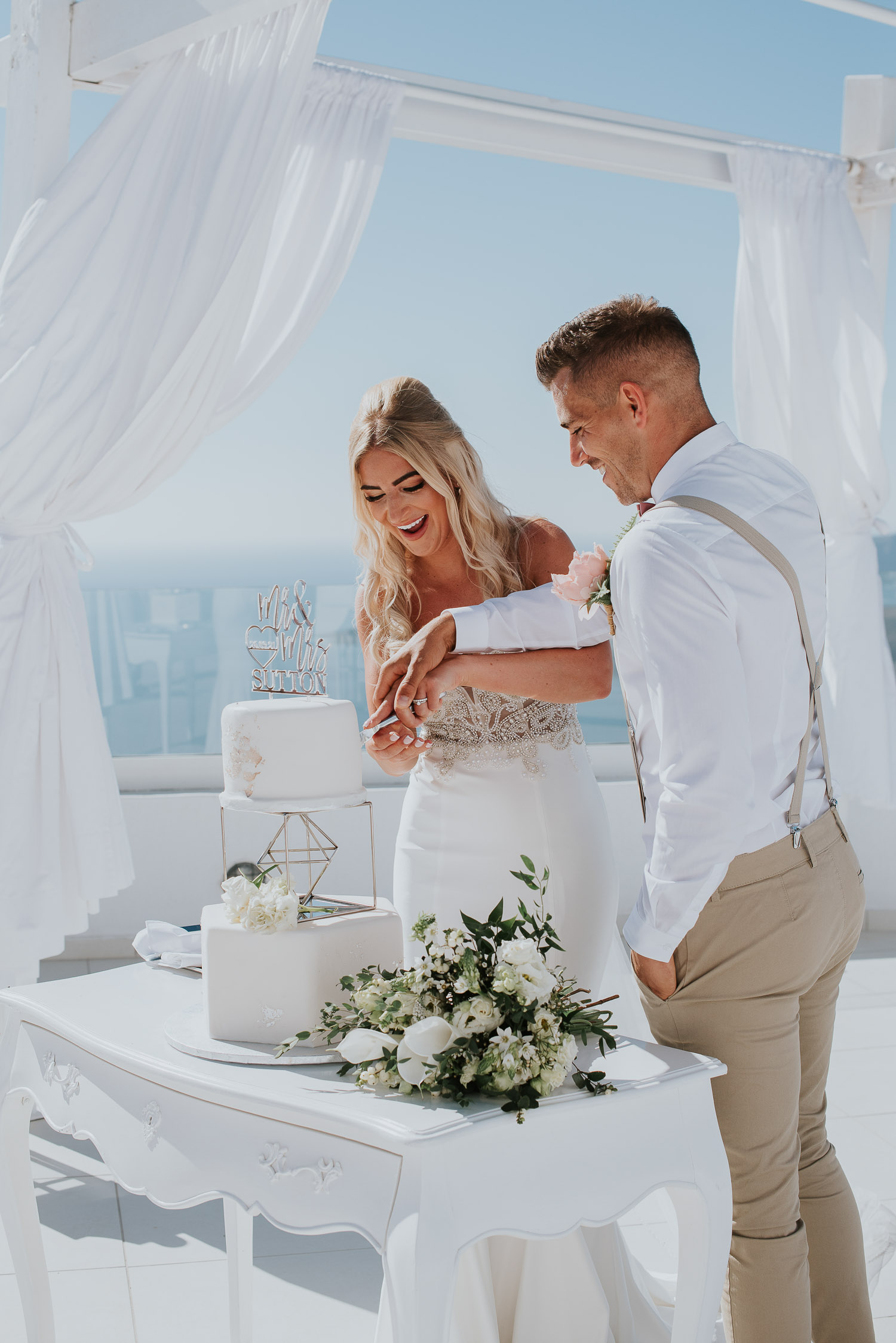 Wedding photographer Santorini: close up of bride and groom laughing as they cut their beautiful cake under gazebo by Ben and Vesna.
