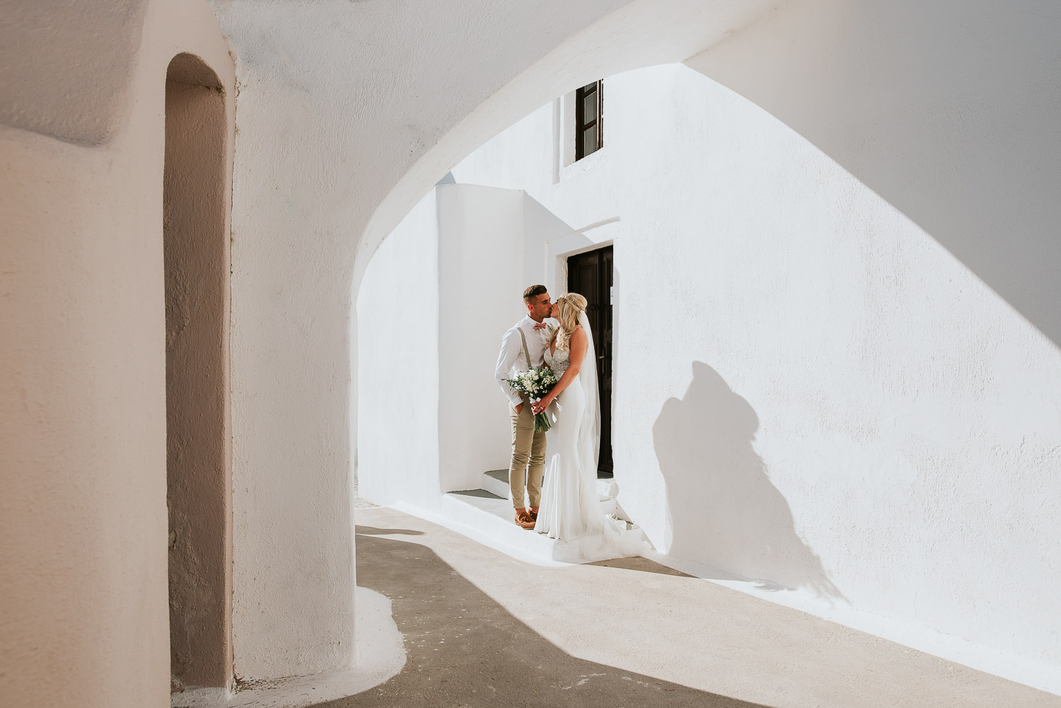 Wedding photographer Santorini: bride and groom kissing under the shapes and shades of Santorini by Ben and Vesna.
