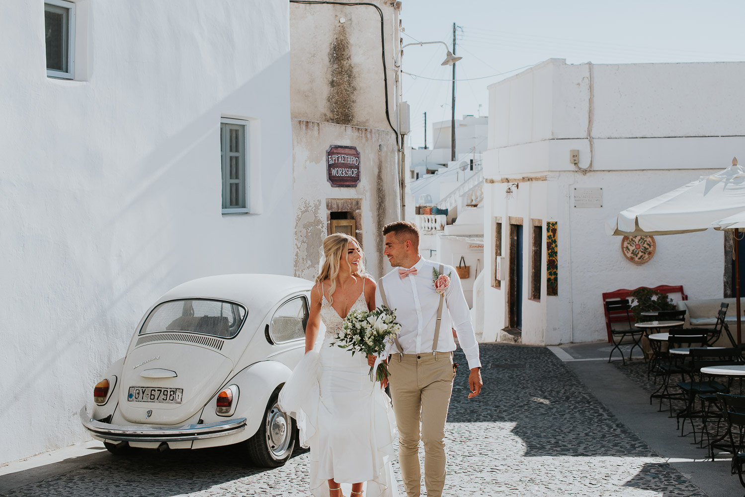 Wedding photographer Santorini: bride and groom walking up the cobbled stone street passing old beetle car  by Ben and Vesna.