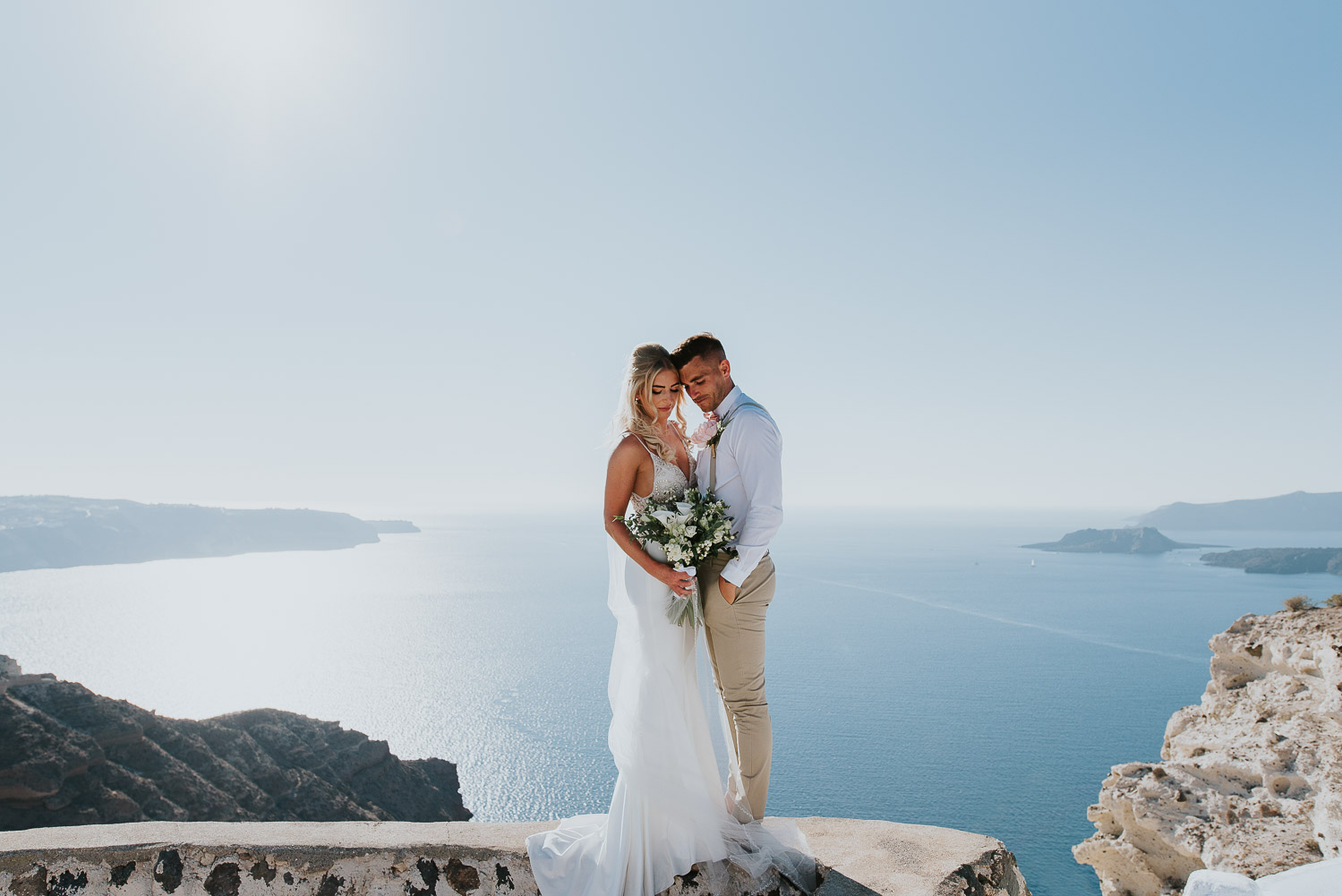Wedding photographer Santorini: panoramic photo of bride and groom surrounded by the sea and the sky behind them by Ben and Vesna.