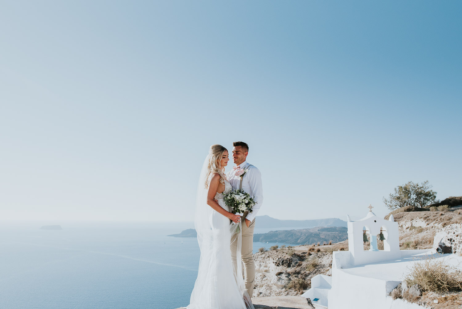 Wedding photographer Santorini: panoramic photo of bride and groom with the sea, sky and the church in the background by Ben and Vesna.