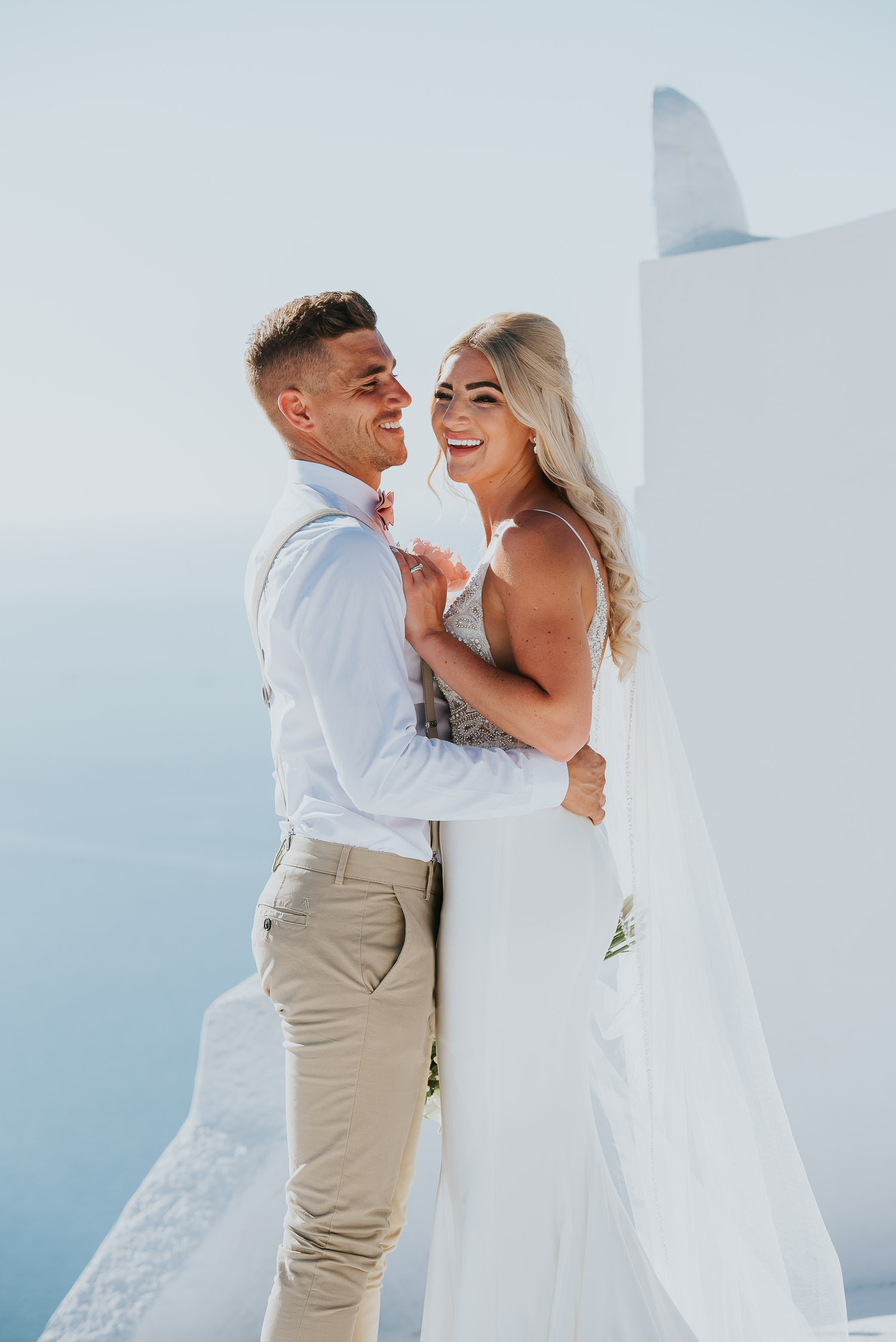 Wedding photographer Santorini: close up of bride and groom laughing in front of the bell tower basked in the afternoon light by Ben and Vesna.