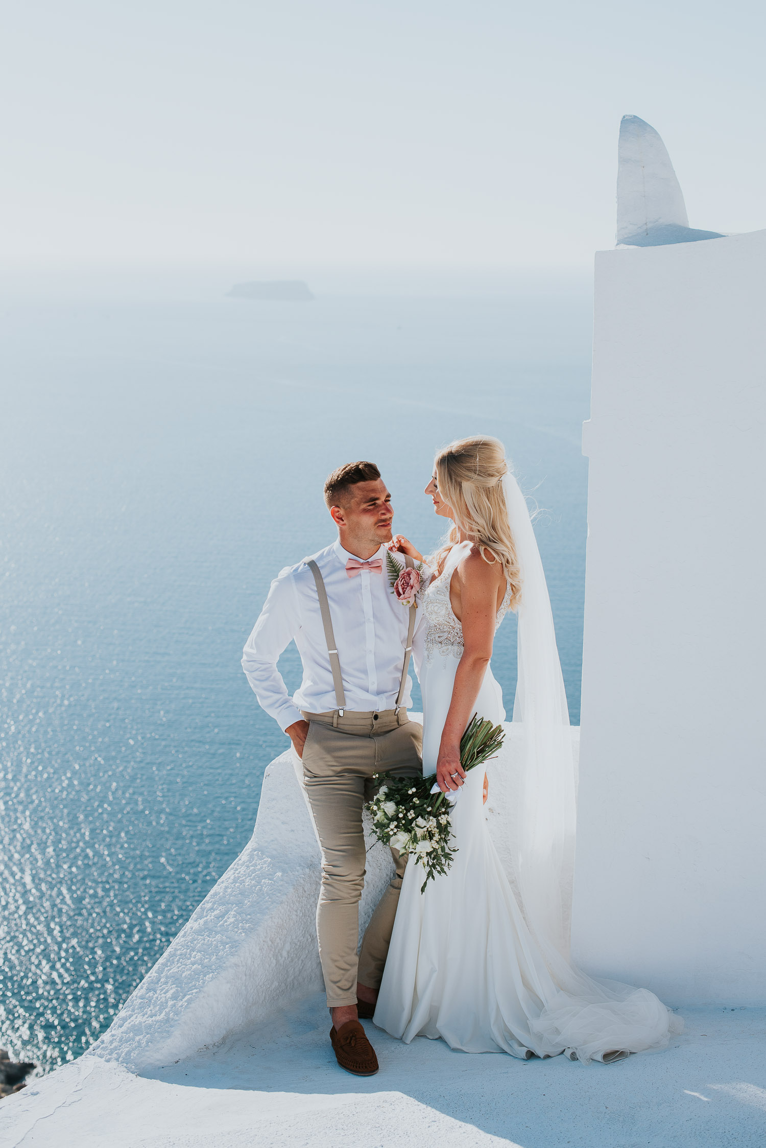 Wedding photographer Santorini: groom and bride next to the bell tower basked in the afternoon light by Ben and Vesna.