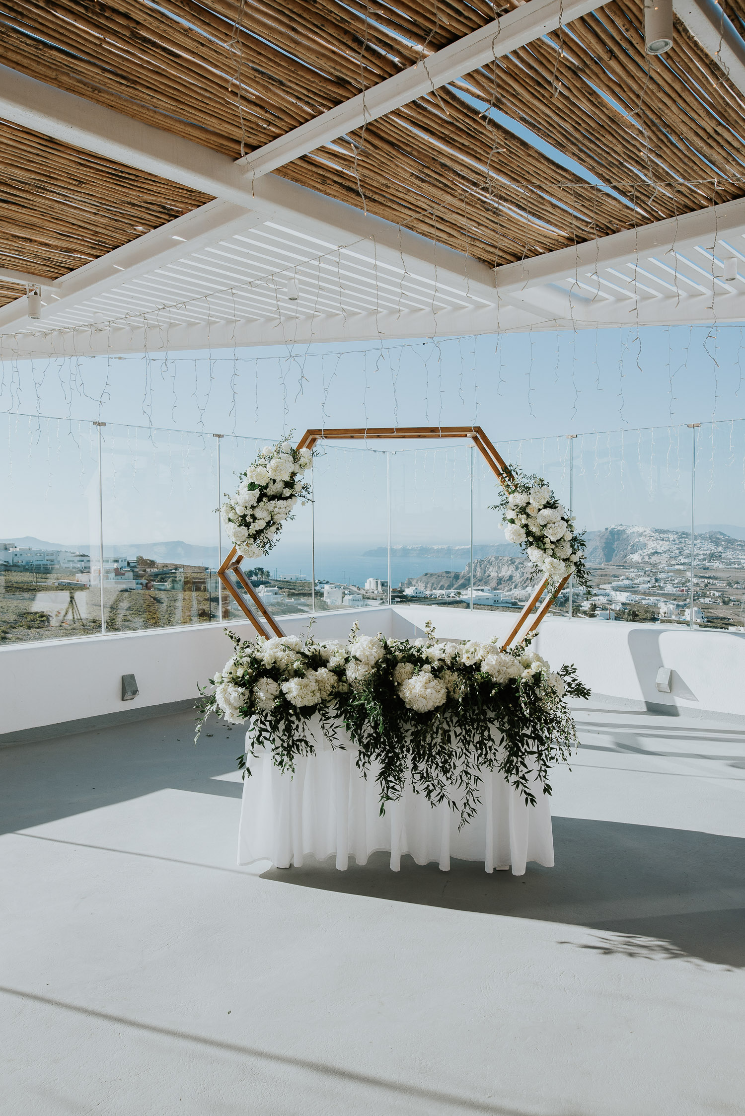 Wedding photographer Santorini: hexagonal wedding arch and the bridal table adorned in floral arrangements basked in the afternoon light by Ben and Vesna.