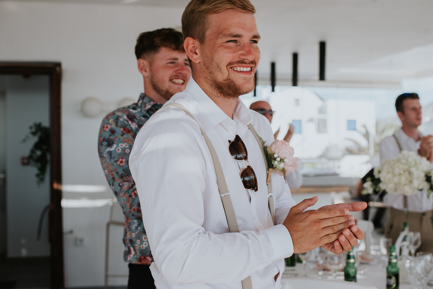Wedding photographer Santorini: close up of guests smiling and clapping as bride and groom enter by Ben and Vesna.