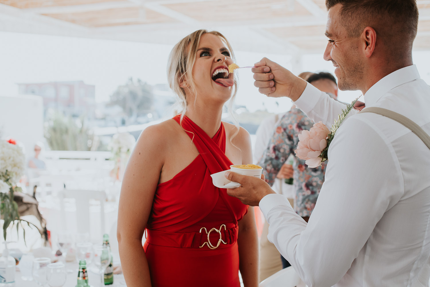 Wedding photographer Santorini: close up of a guest pulling faces as groom feeds her ice cream by Ben and Vesna.
