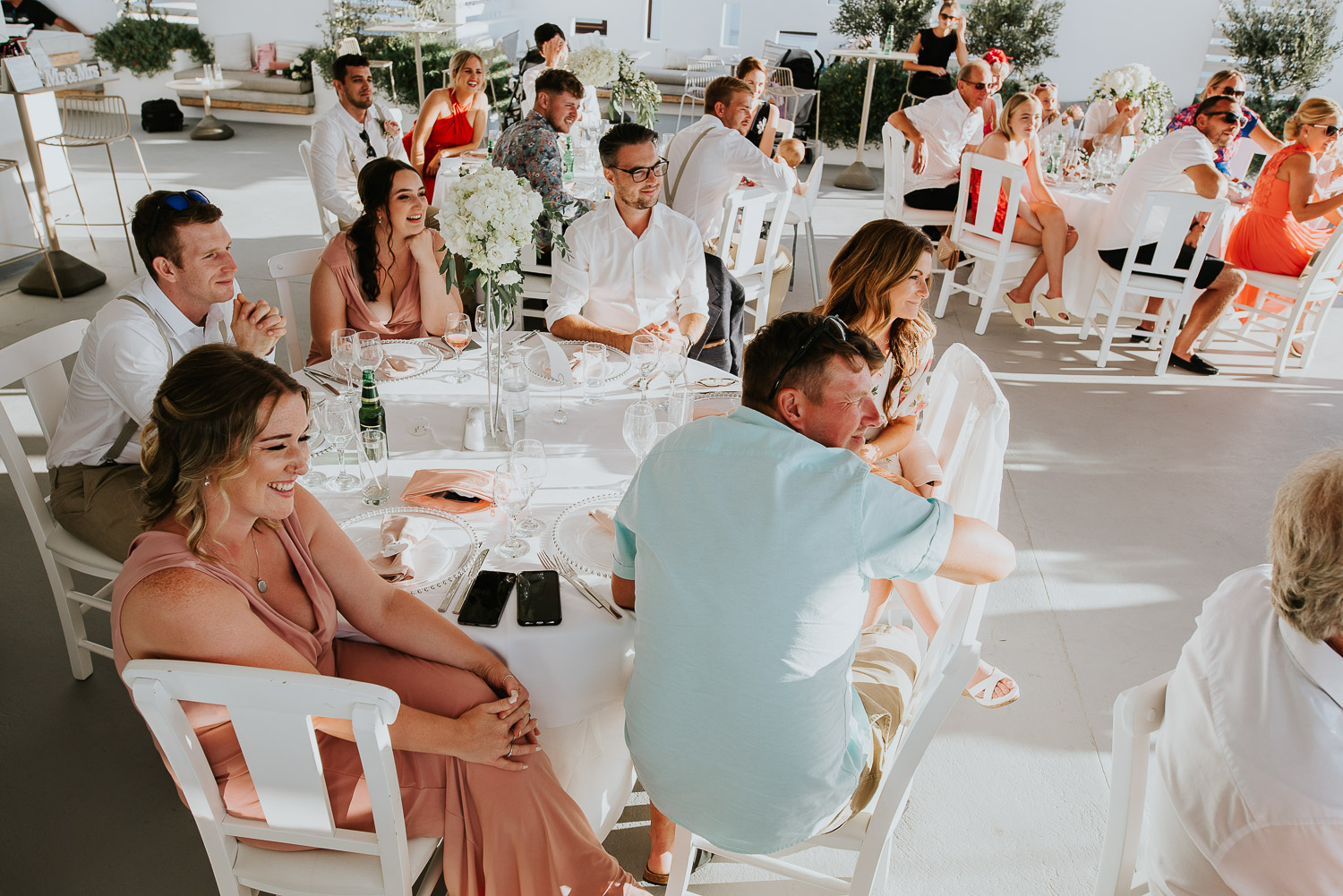 Wedding photographer Santorini: guests sat at their table laughing  as they listen to the speeches by Ben and Vesna.