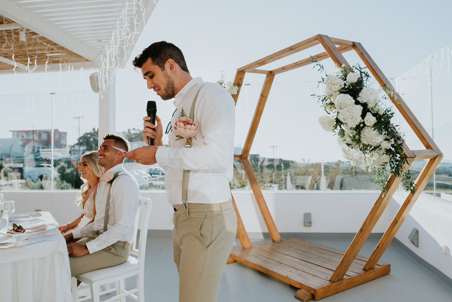 Wedding photographer Santorini: bride and groom laugh as they listen to the best man's speech by Ben and Vesna.