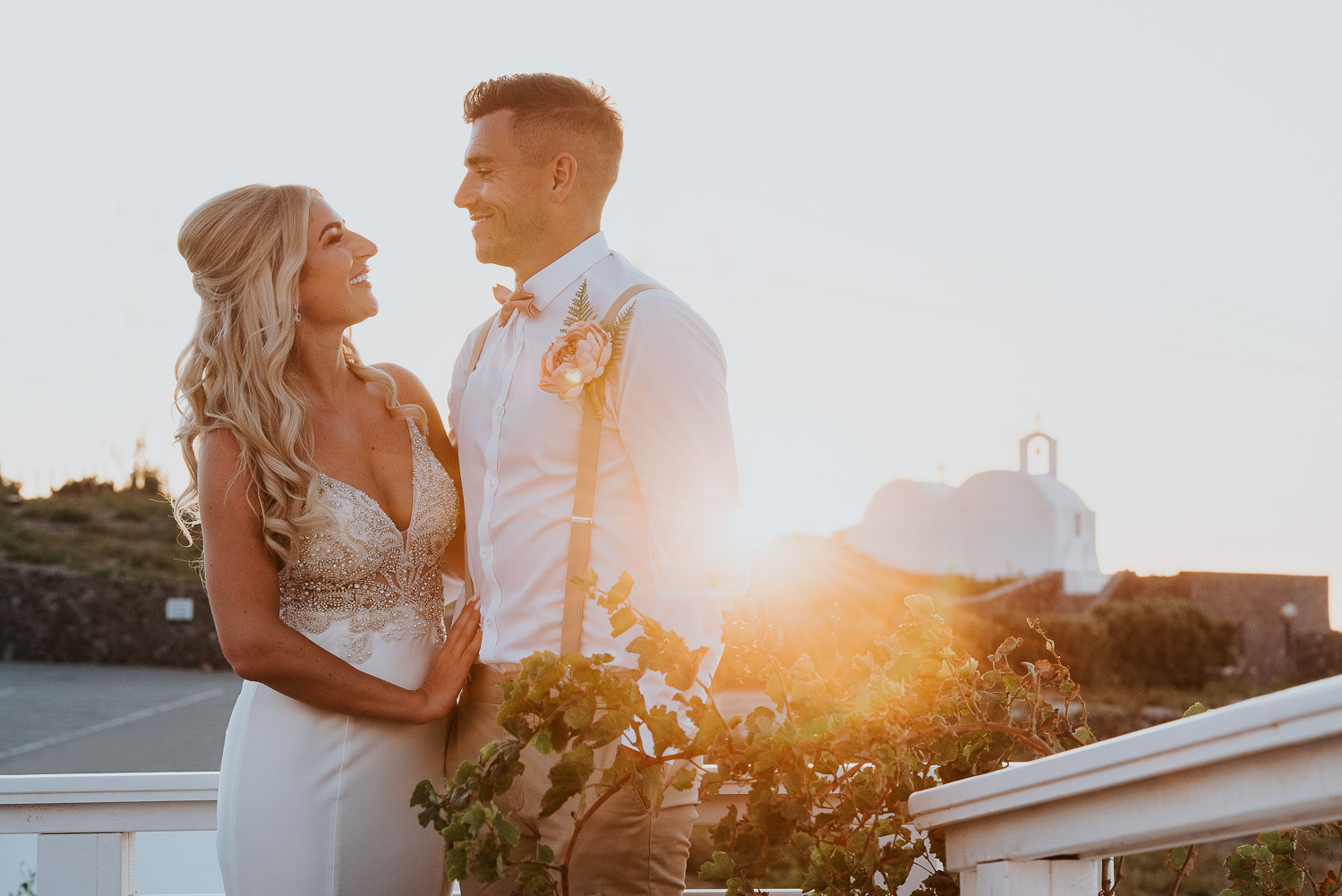Wedding photographer Santorini: bride and groom embraced in the golden sunset light with a church in the background by Ben and Vesna.