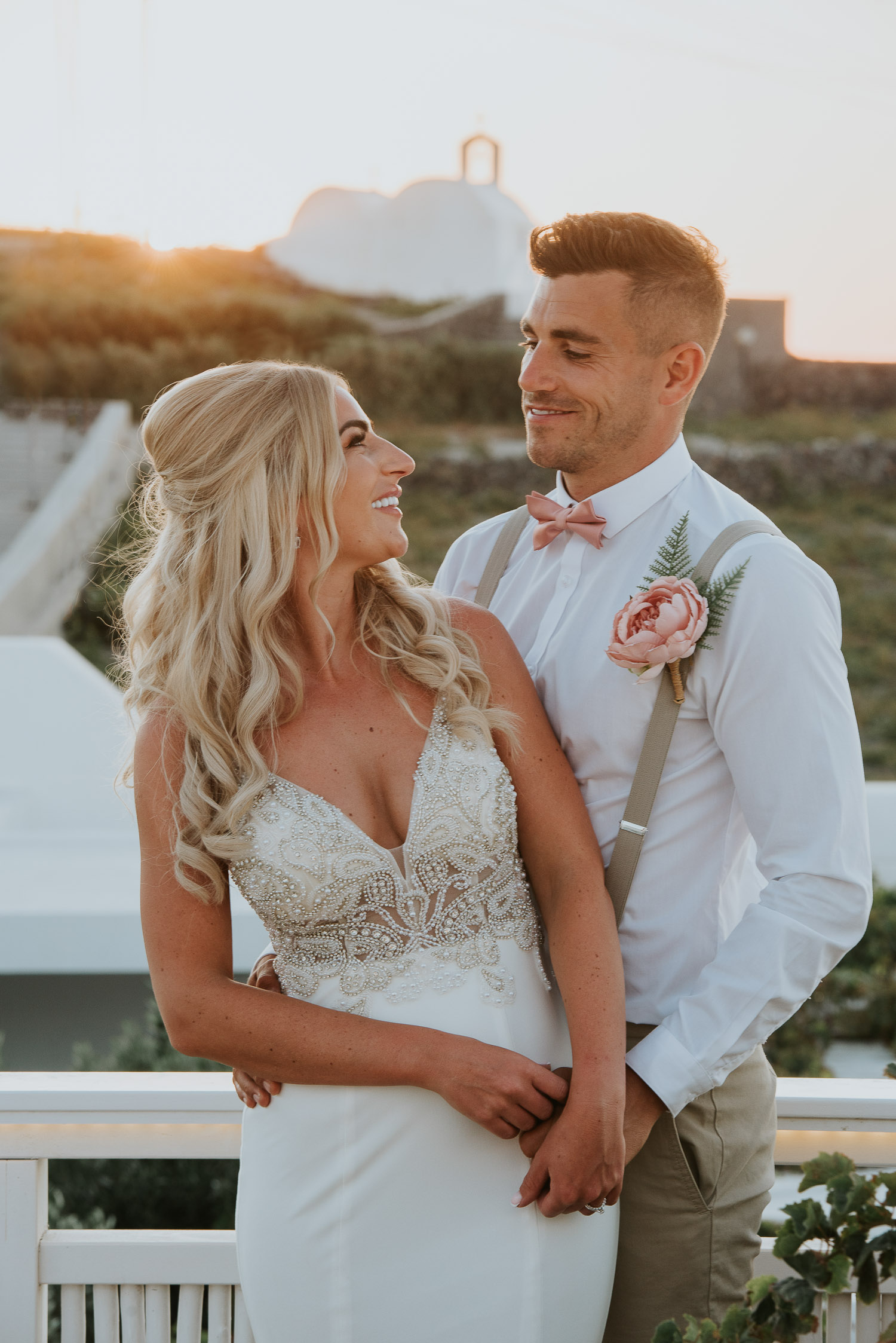 Wedding photographer Santorini: close up of bride and groom smiling backlit by golden sunset light with a church in the background by Ben and Vesna.