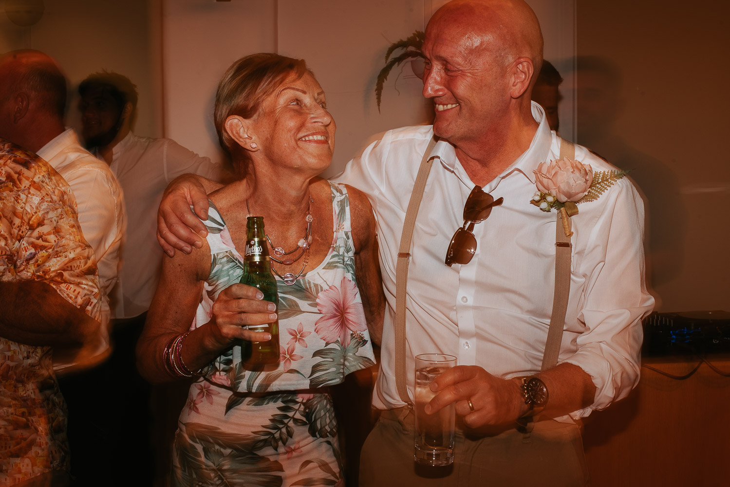 Wedding photographer Santorini: close up of a wedding guest couple smiling with drinks in their hands by Ben and Vesna.