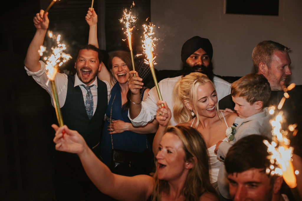 Mykonos wedding photographer: wedding guests waving sparklers in the air at the club.