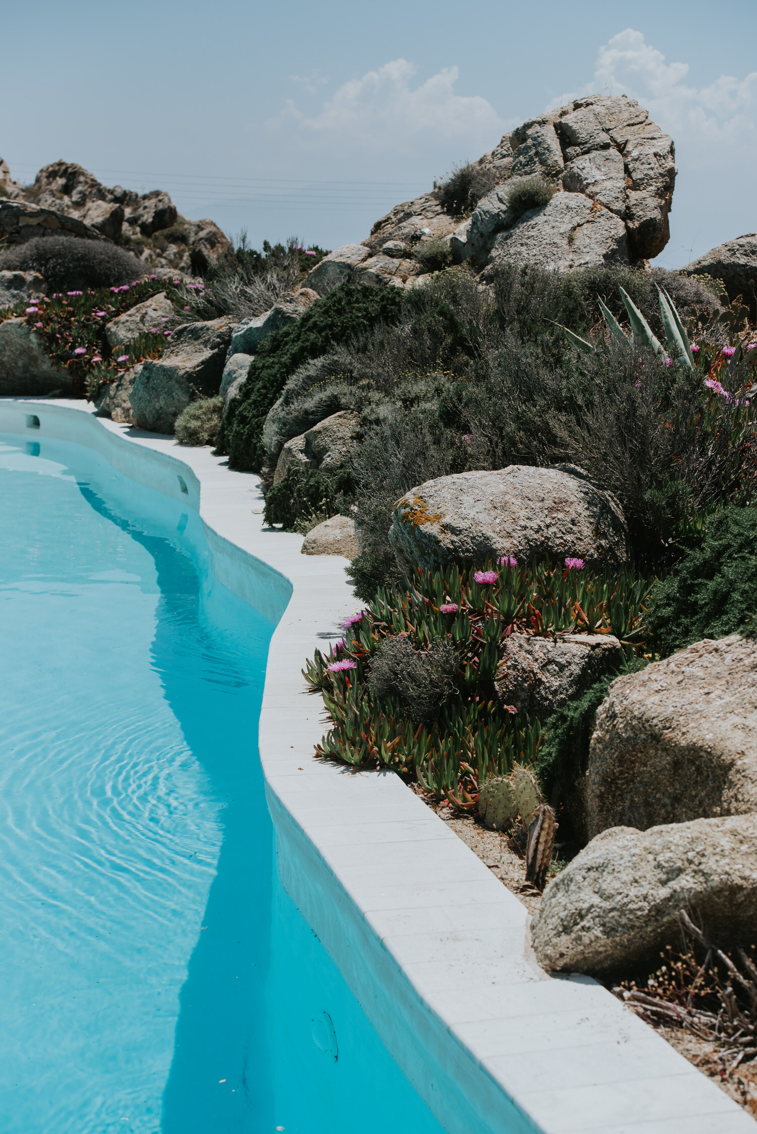 Mykonos wedding photographer: turquoise pool water surrounded by Mykonian rocks and wild herbs.