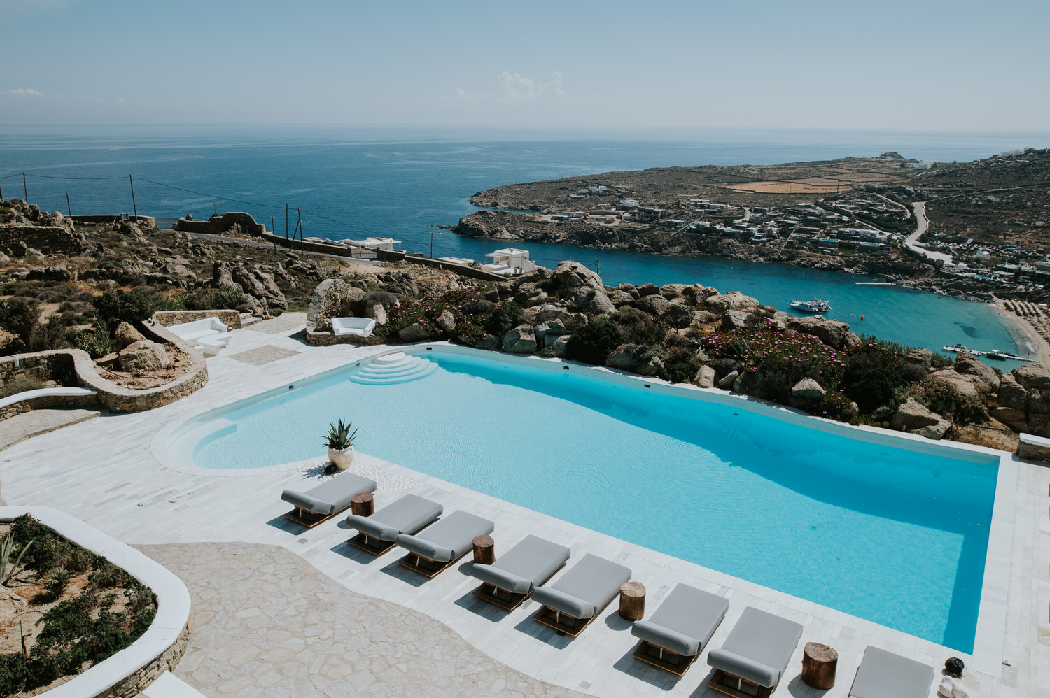 Mykonos wedding photographer: beautiful large pool surrounded by Mykonian rocks with the beach views and the sea in the background.