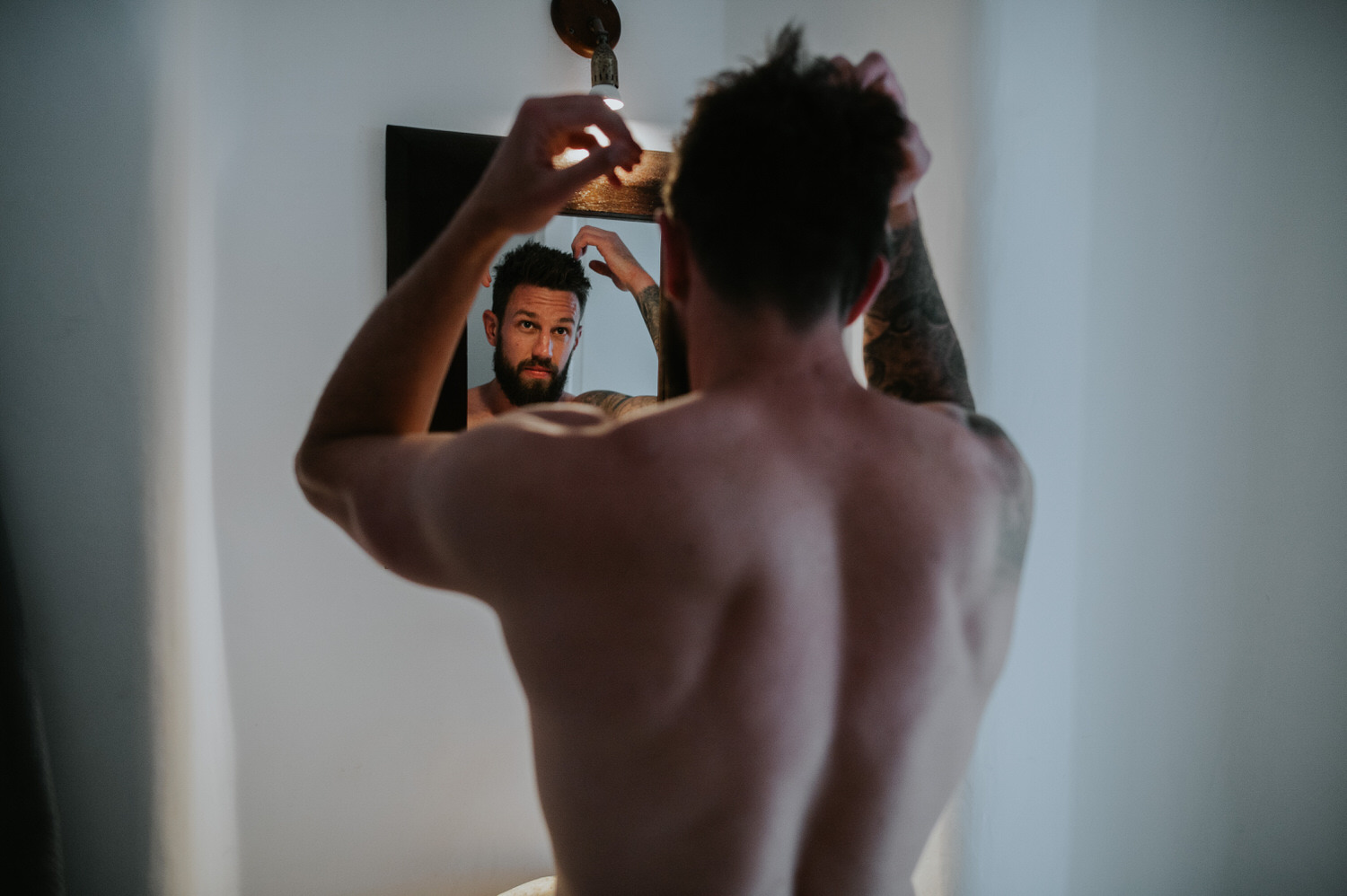 Mykonos wedding photographer: shirtless groom looking in the mirror fixing his hair.