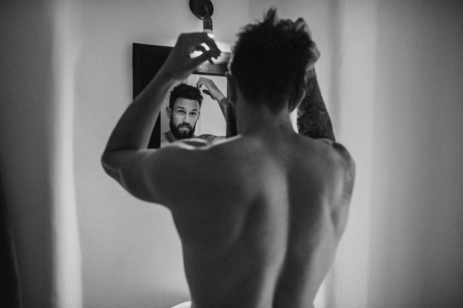 Mykonos wedding photographer: black and white portrait of shirtless groom looking in the mirror fixing his hair.