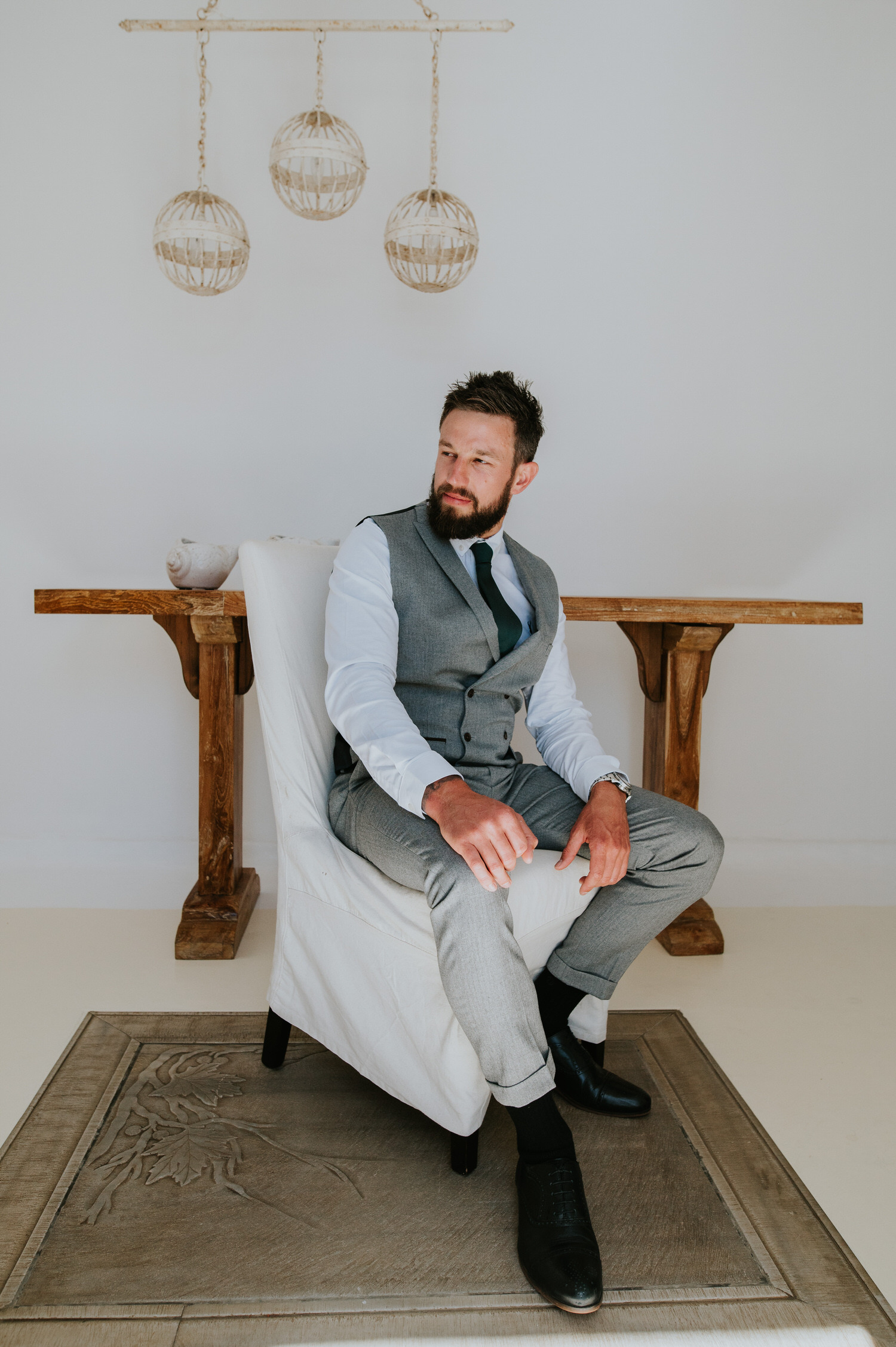 Mykonos wedding photographer: suited groom looking handsome sat at the chair in the villa.