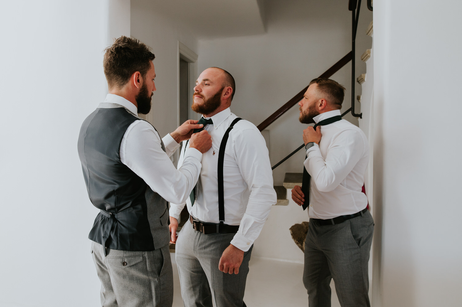 Mykonos wedding photographer: handsome groom helping his best man with the tie as they get ready.