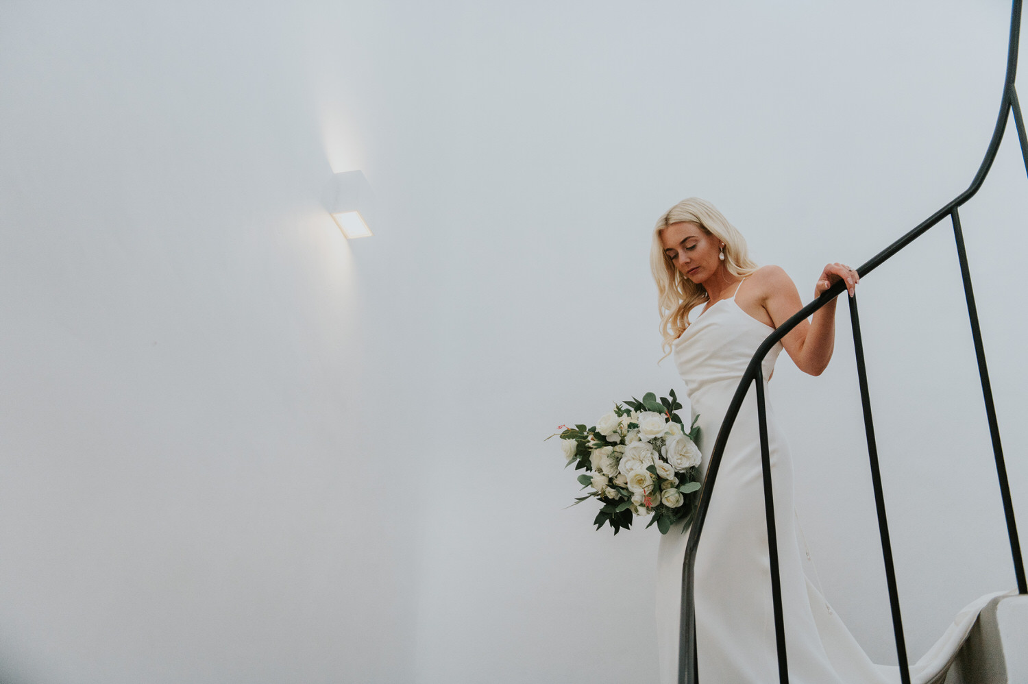 Mykonos wedding photographer: gorgeous bride walking down the spiral stairs in villa holding her bouquet.