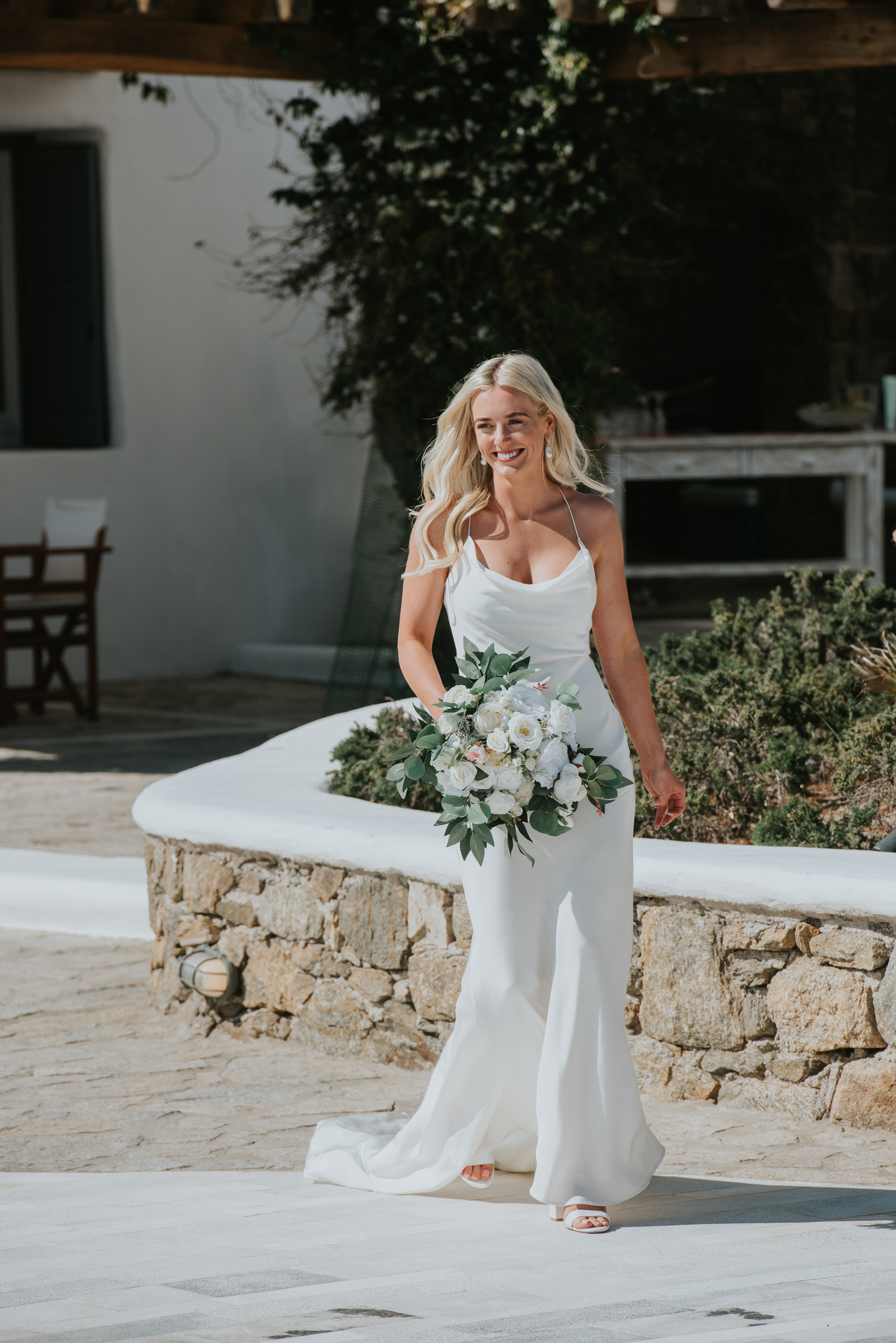 Mykonos wedding photographer: gorgeous bride walking with a wide smile on her face and the dress in the wind as she walks.
