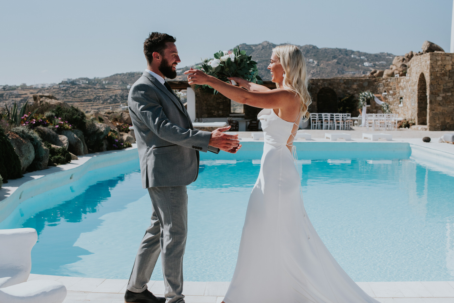 Mykonos wedding photographer: close up of bride and groom going for a hug during first look next to the pool and the rocks in the background.