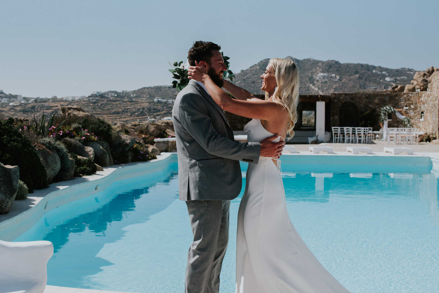 Mykonos wedding photographer: close up of bride reaching out to her groom next to the pool and the rocks in the background.