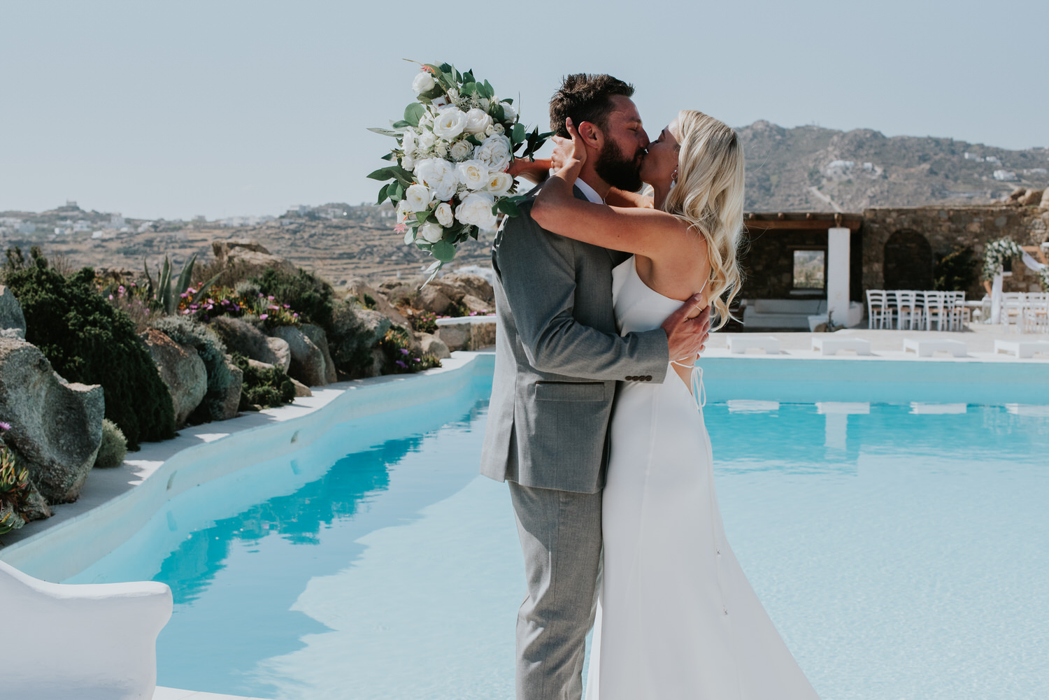 Mykonos wedding photographer: close up of bride and groom embraced in a kiss next to the pool and the rocks in the background.