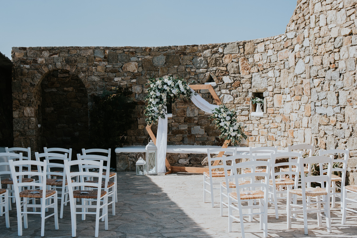 Mykonos wedding photographer: panoramic photo of the wedding ceremony terrace and the floral arch against the rocky wall.