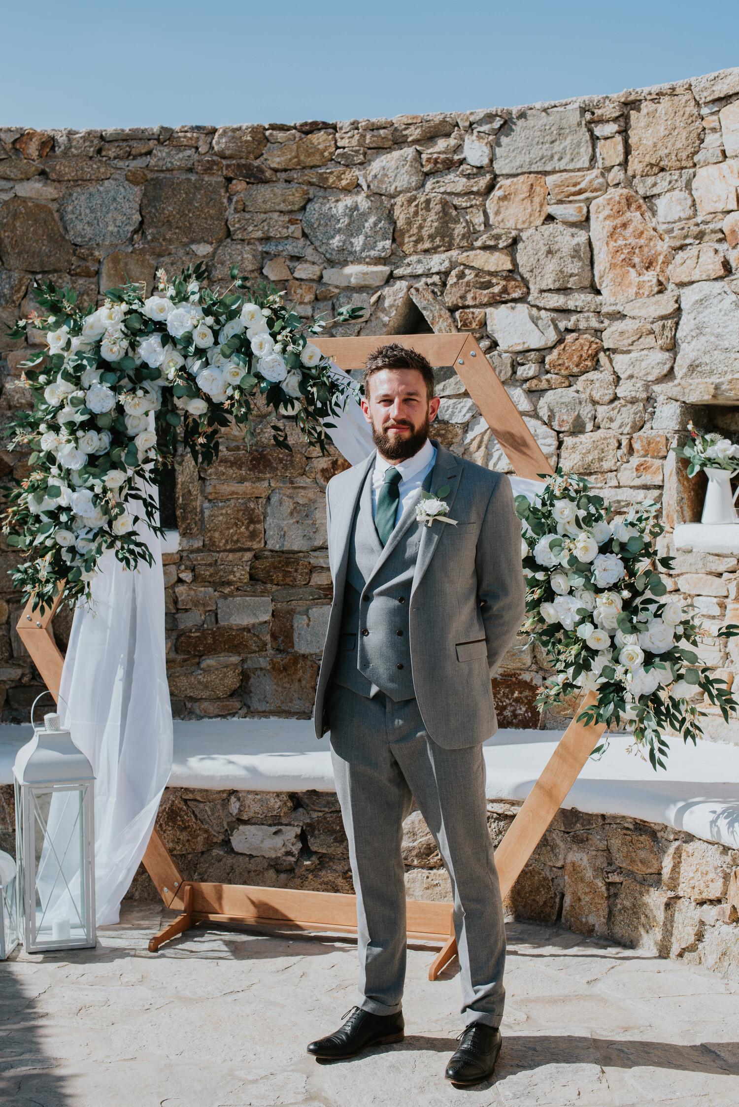 Mykonos wedding photographer: groom looking handsome standing in front of the floral arch.