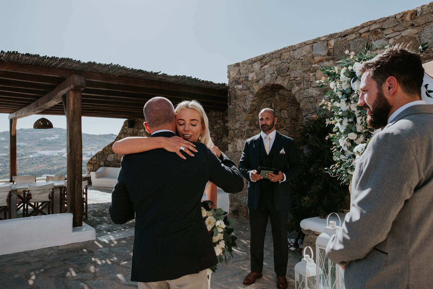 Mykonos wedding photographer: bride hugging as she comes up the aisle with groom and celebrant around.