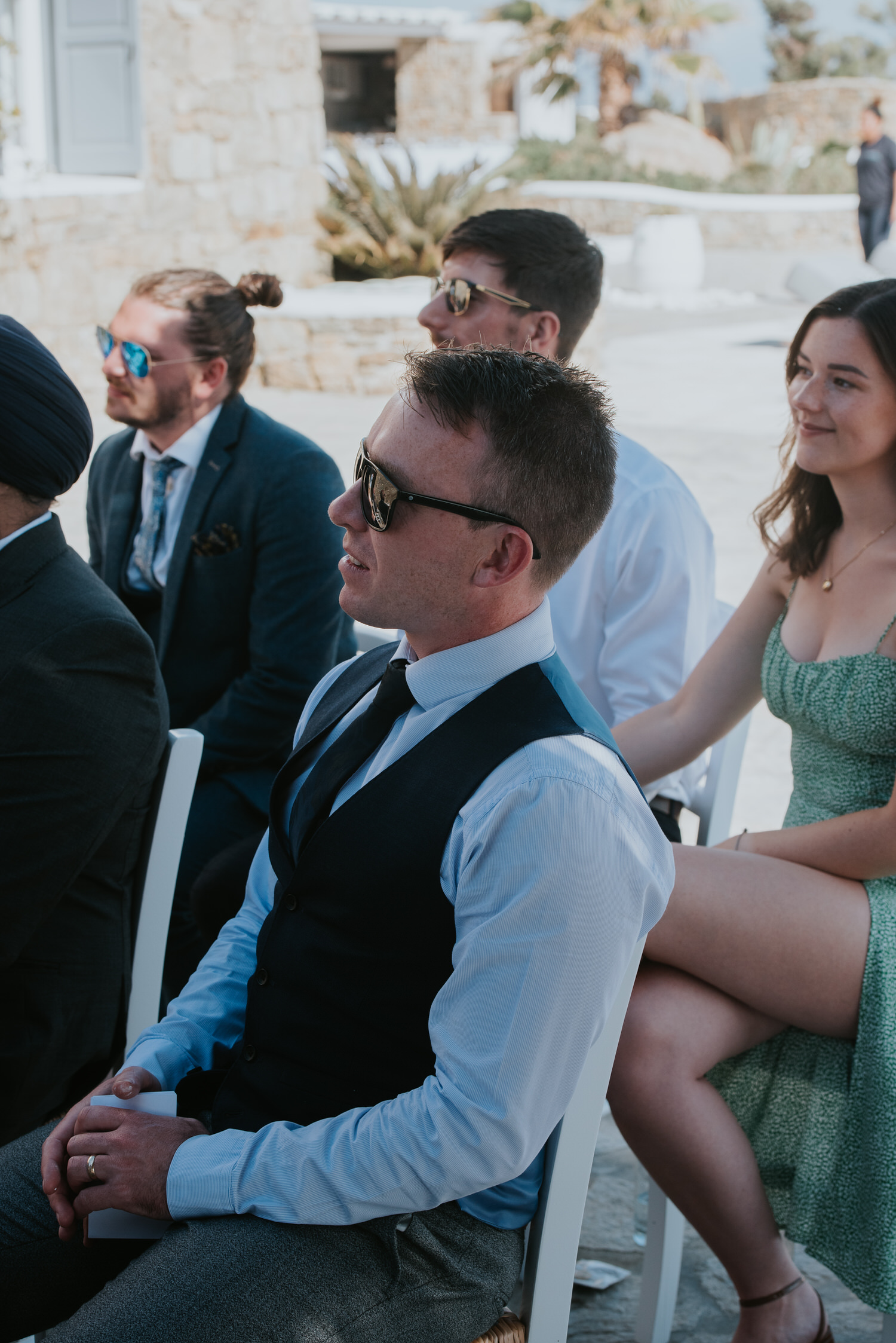 Mykonos wedding photographer: close up of guests sat in the shade enjoying the ceremony.