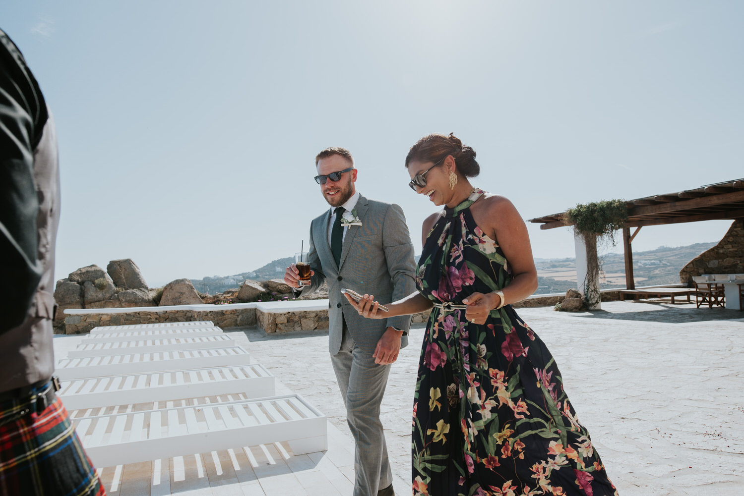 Mykonos wedding photographer: landscape photo of guests walking pass smiling in the afternoon sun.