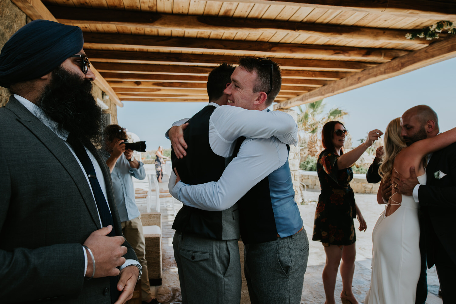 Moment bride and groom were both hugging friends receiving congratulations with Mykonos wedding photographer in the background.