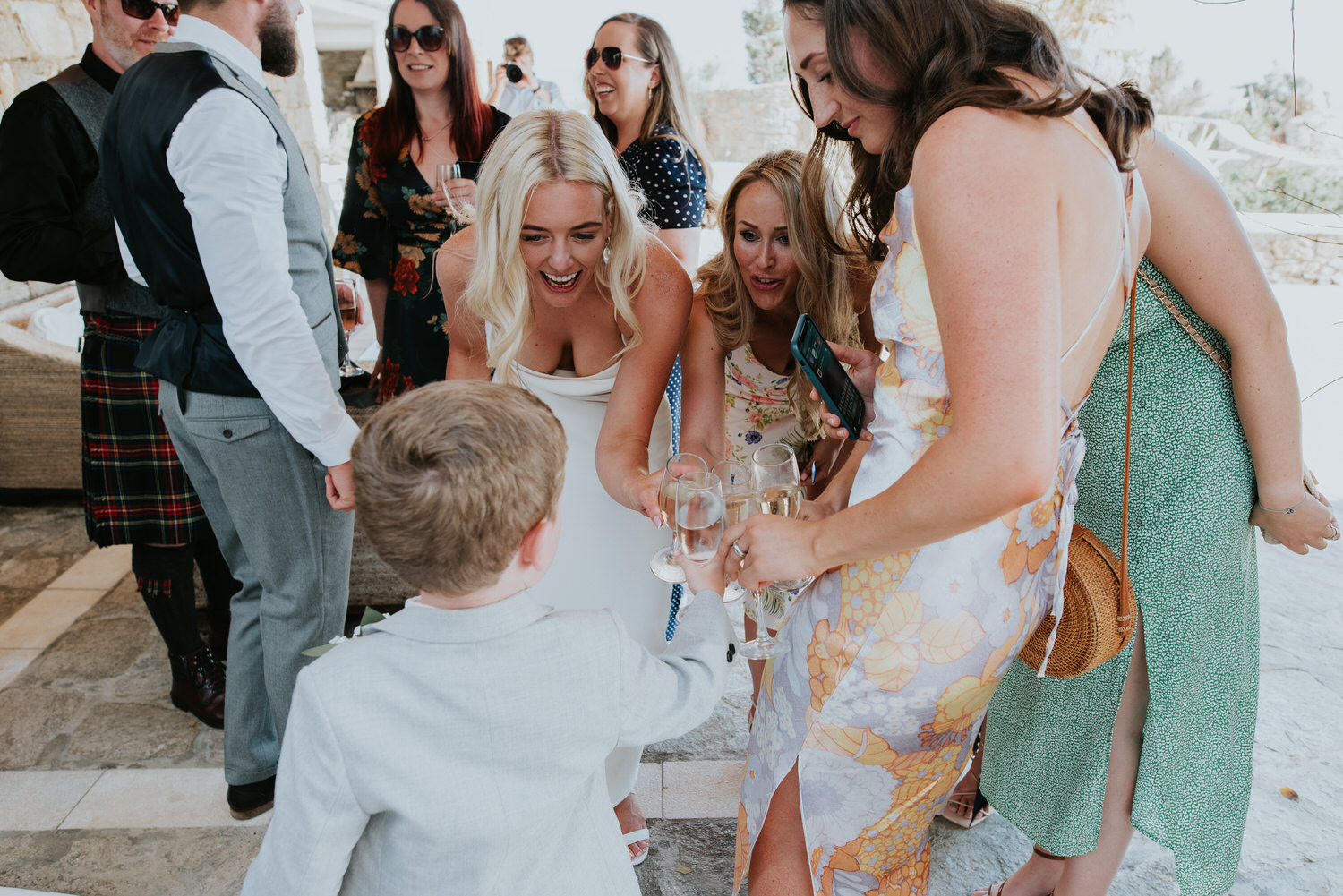 Mykonos wedding photographer: bride and friends smiling clinking glasses with the little boy.