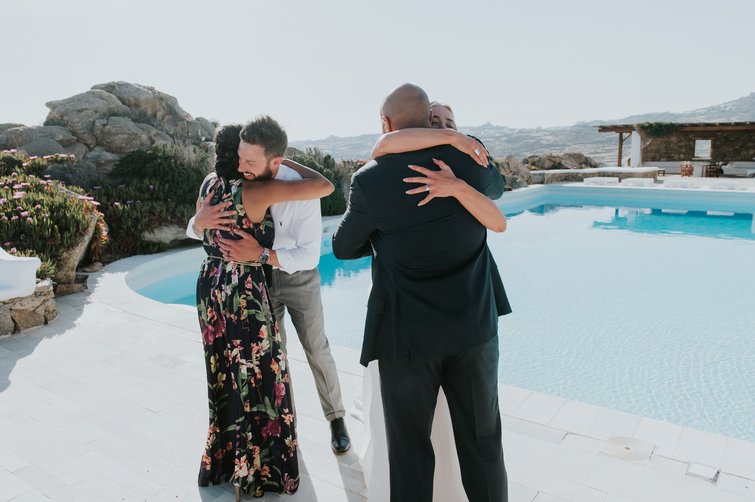 Mykonos wedding photographer: bride and groom hugging their friends next to the pool in afternoon light.